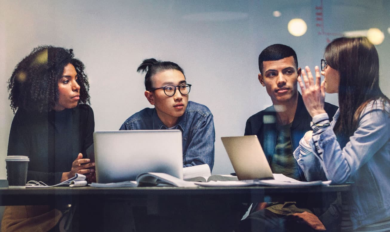 four students in a discussion with laptops open