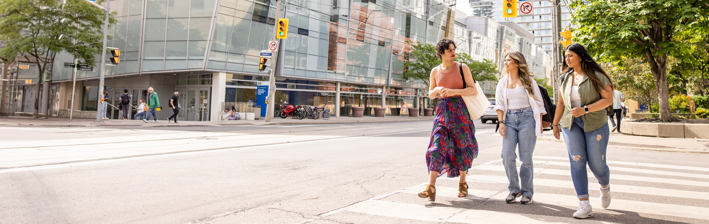 Three students chat while crossing the street on campus.