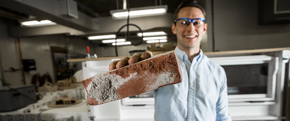 A student wearing protective glasses holds a brick