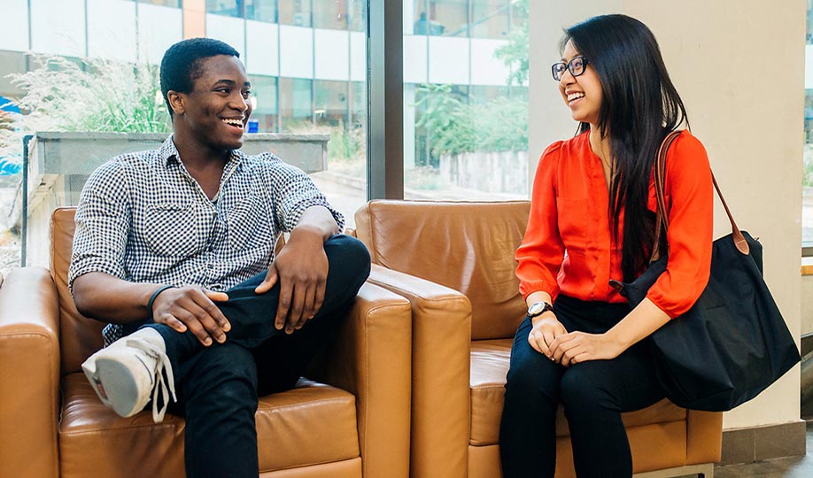 Two students chat on brown sofa chairs