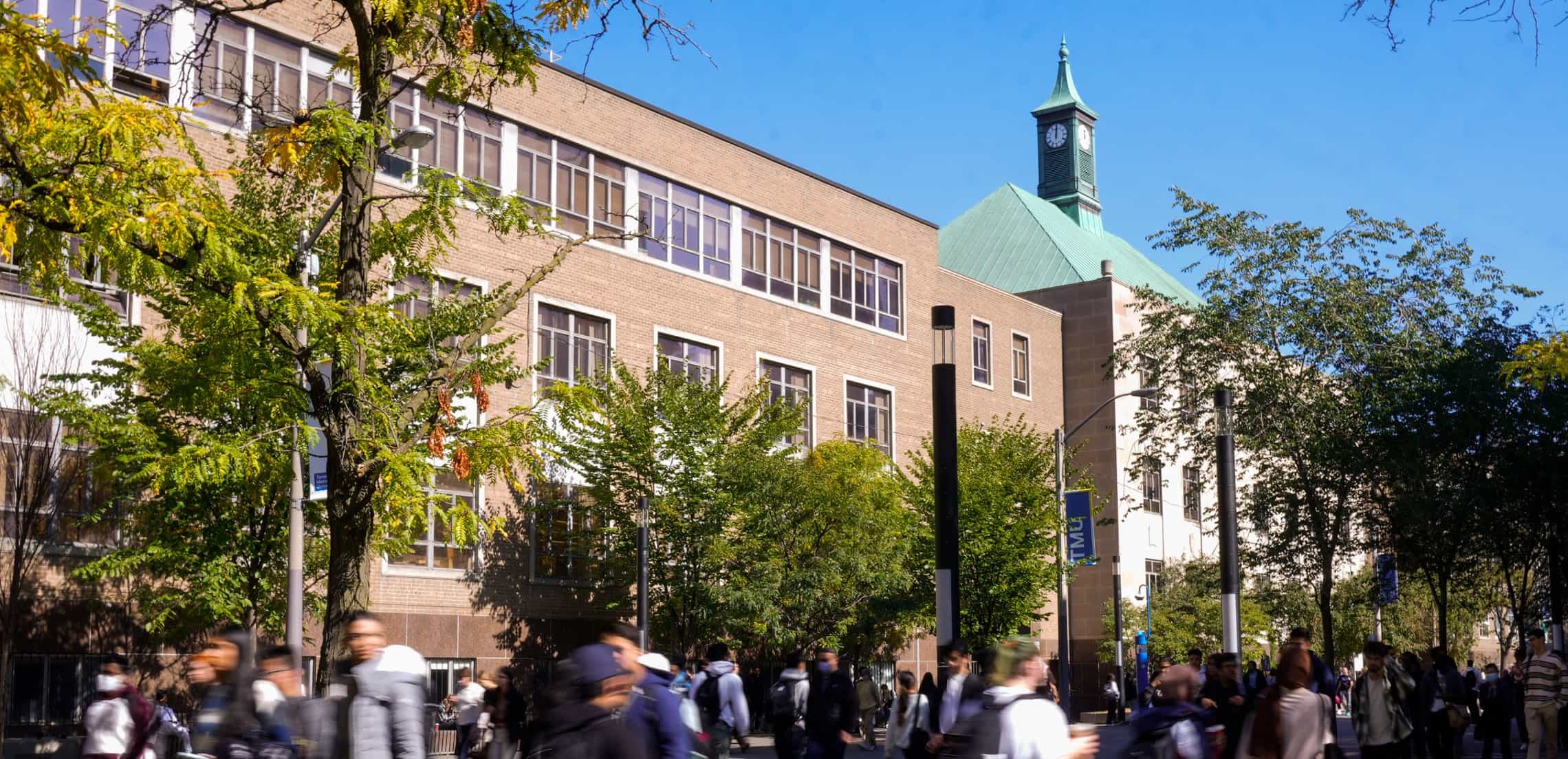 A bustling street on campus with pedestrians in motion, their movements blurred as they walk to their destinations.