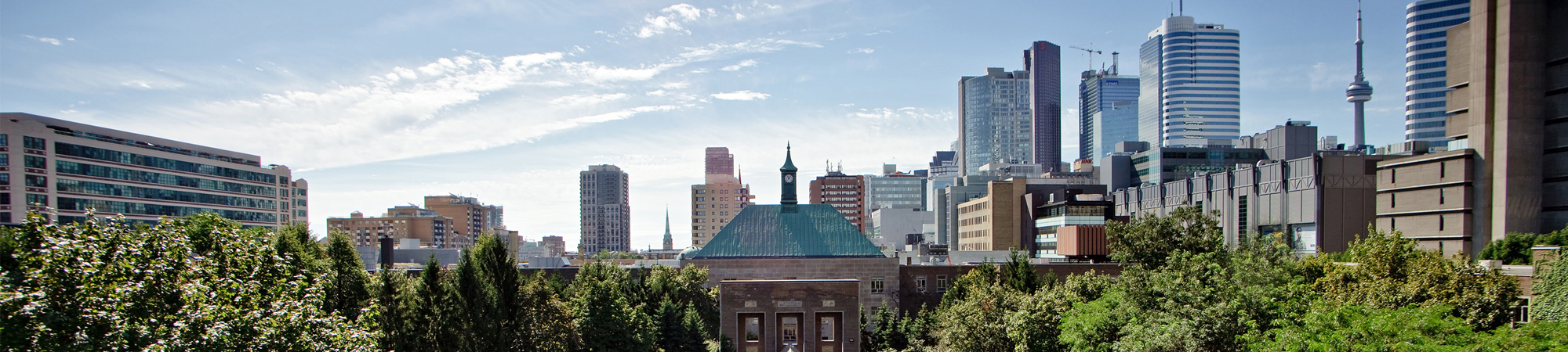 Warm sunny day looking at luscious green trees around Kerr Hall clock tower with the Toronto skyline in the background. 