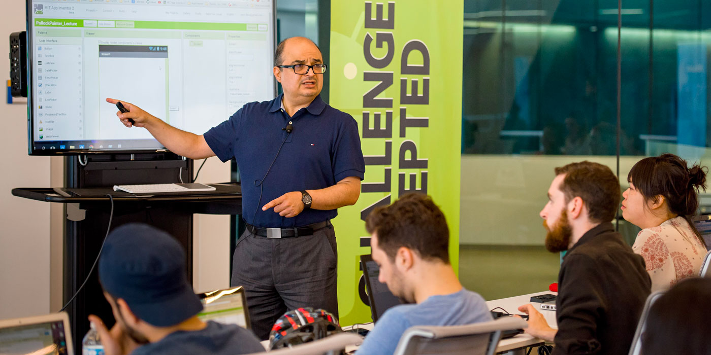 A Ryerson instructor point to a screen in front of an intimate class of students. 