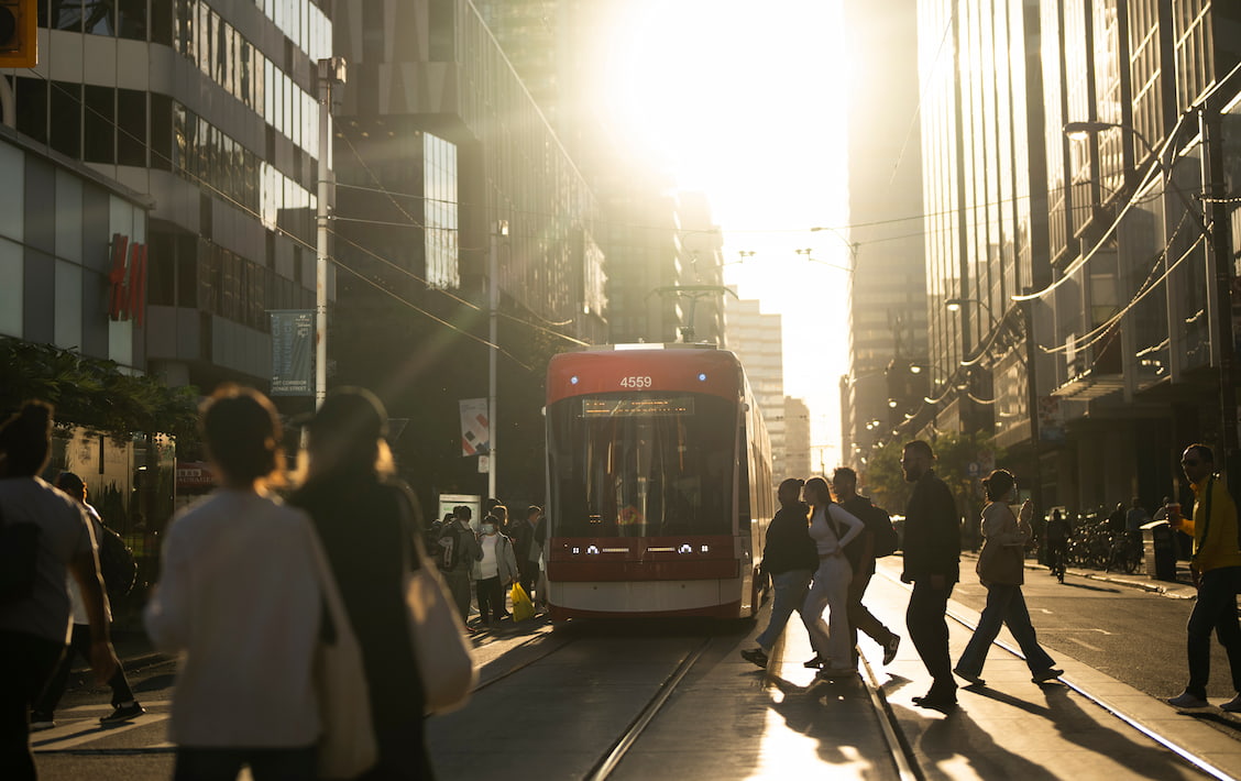 a busy intersection near campus with a streetcar in view and lots of people crossing