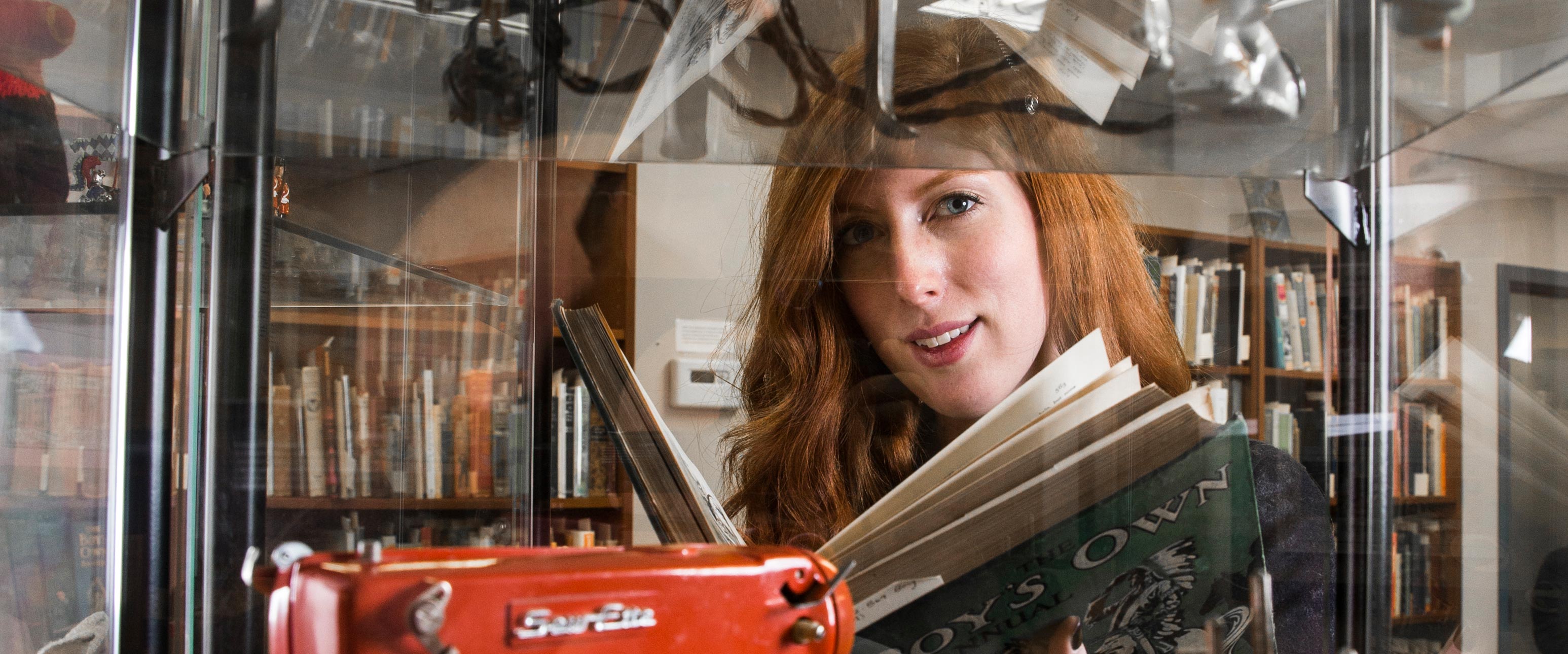 Graduate student reading a book next to a glass display case containing a sewing machine