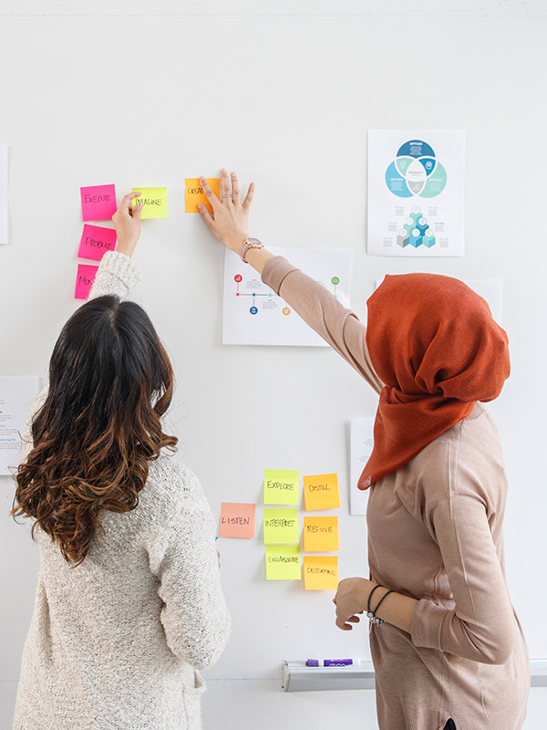 Two students brainstorm ideas together on a whiteboard.