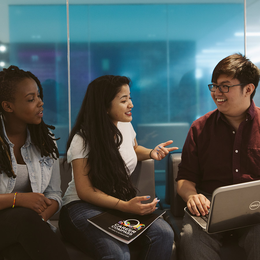 Three students laughing as they work on a laptop.