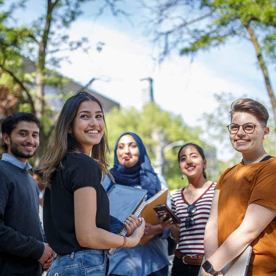 A group of students smile together. Behind them is the outline of the Kerr Hall clocktower on a sunny day.