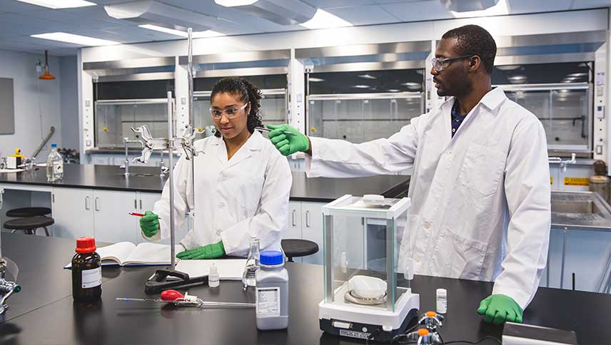 Two students working in a chemistry lab. They are both wearing the appropriate protective safety equipment. 