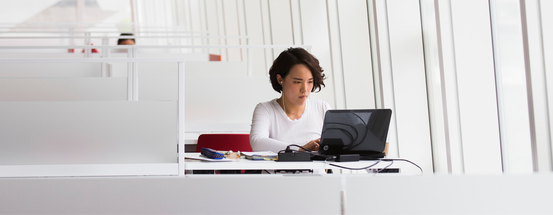 A woman working at a white desk, surrounded by white metal dividers in the SLC.