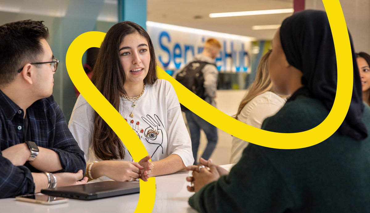 Two students speaking with an advisor in the ServiceHub. Other students can be seen in the background.