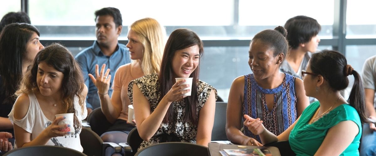 Graduate students chat holding coffee cups.