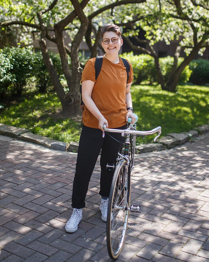 A student poses with her bike. She is smiling and looking at the camera.