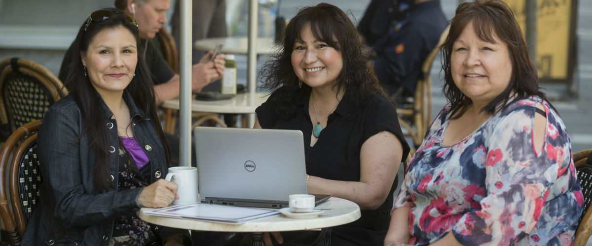 Three Indigenous women sit at a patio on the TMU campus