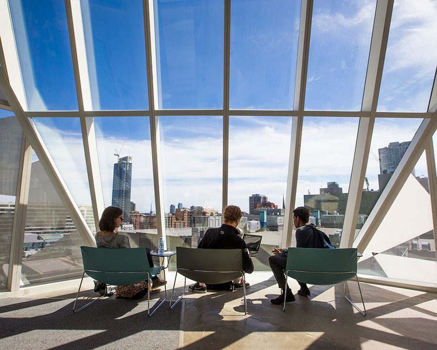 Three students sitting on chairs in the SLC, facing a giant window overlooking the Toronto skyline. Their backs are toward the camera.