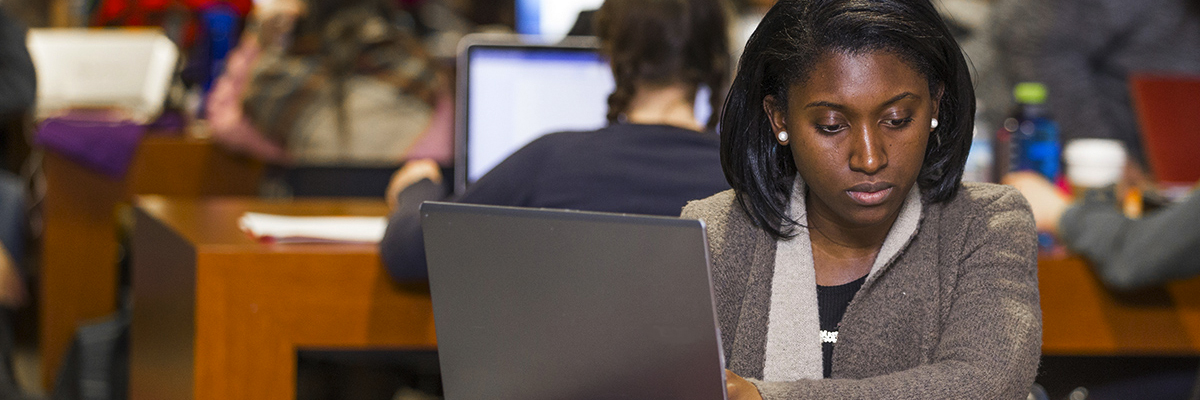 A student on their laptop in a workspace with other students around.