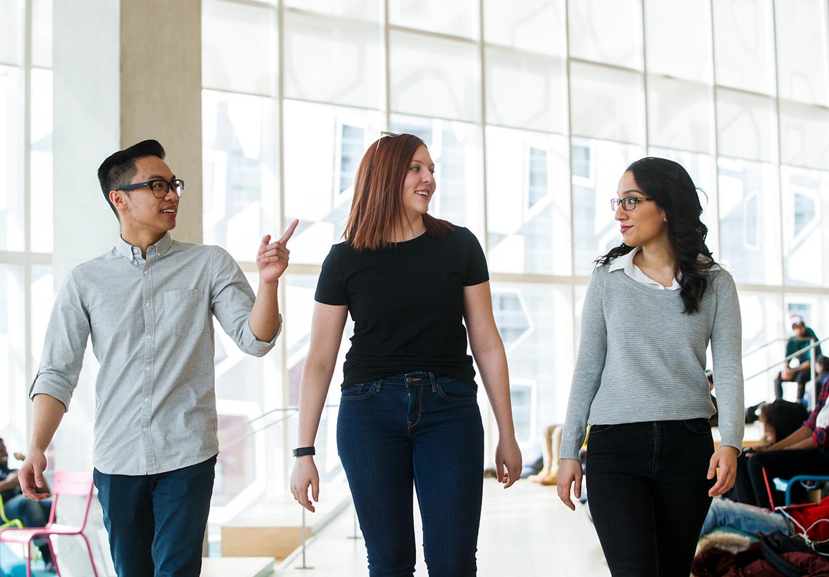 Three students walk and talk on campus.