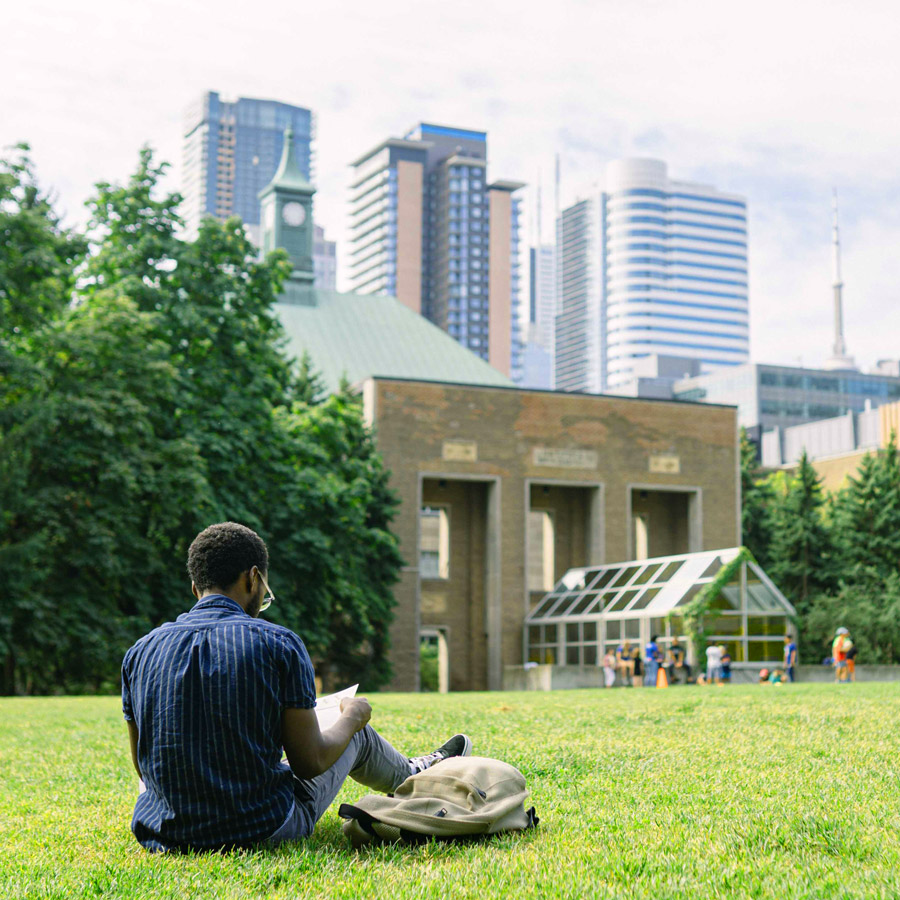 A student sits and reads a book in the Quad on a sunny day.