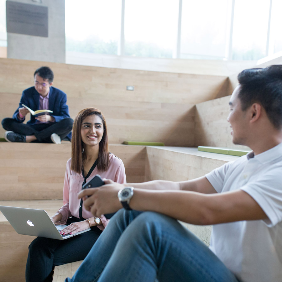 Students with books and a laptop working on the stairs in the SLC lobby.