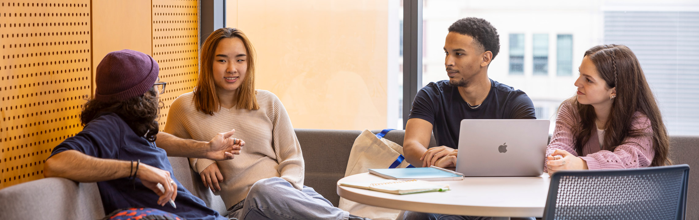 Four students chat animatedly around a table in the library.