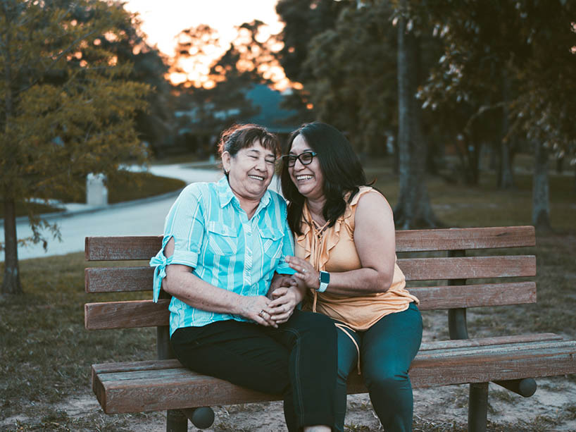 An older woman and younger woman laugh on a park bench.