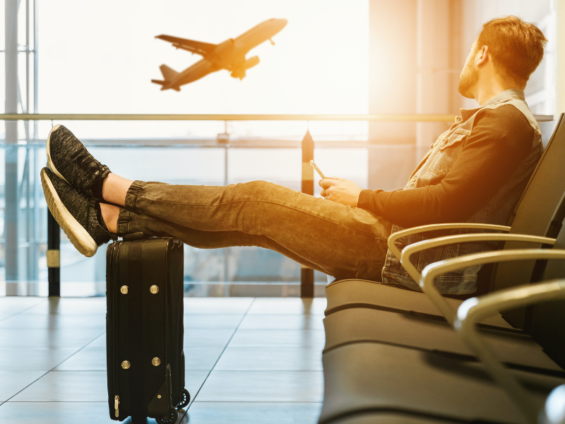 Person sitting in airport looking out of window at plane in flight.